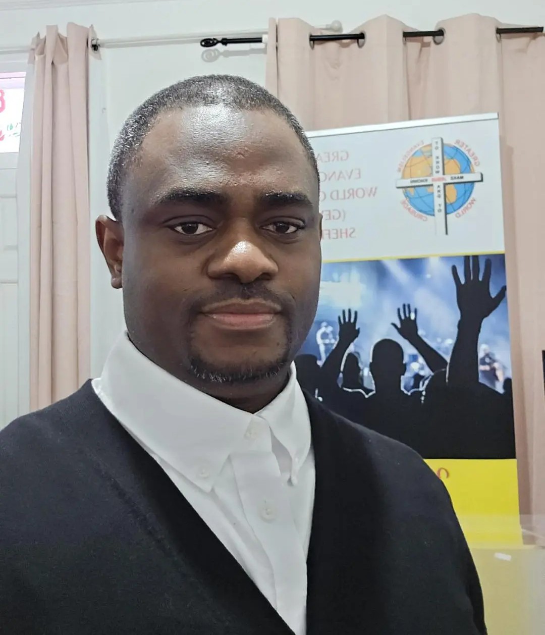 Pastor Timothy Igani wearing formal attire, smiling warmly at the camera. Professional headshot against a neutral background, conveying approachability and pastoral warmth